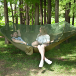 Two-person camping hammock with mosquito net set up between trees in a forest